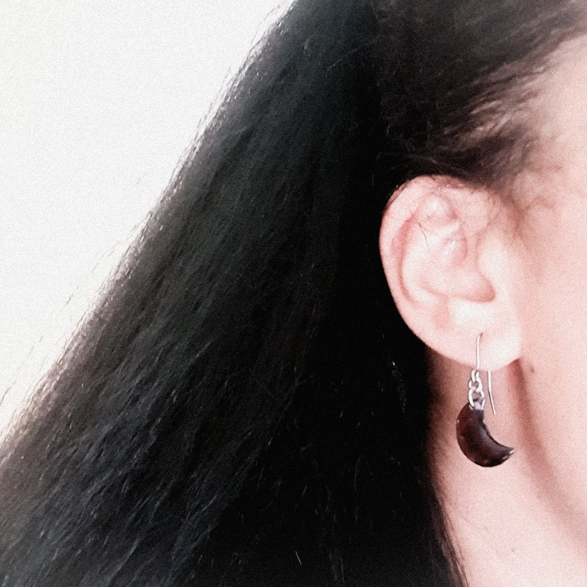A pair of Artemis moon drop earrings, shown being worn. The wearers face is out of shot with hair pulled back to display the earring. 