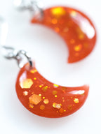 Close up of the Artemis moon drop earrings in orange with holographic colour shifting glitter on a white background