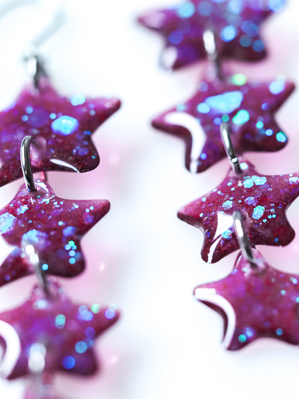 Close up of Astrea star drop earrings in purple iridescent glitter on a white background
