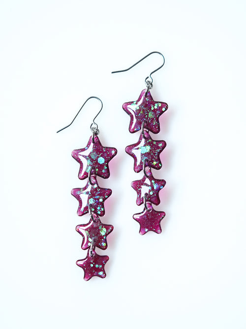 Astrea star drop earrings in purple iridescent glitter on a white background