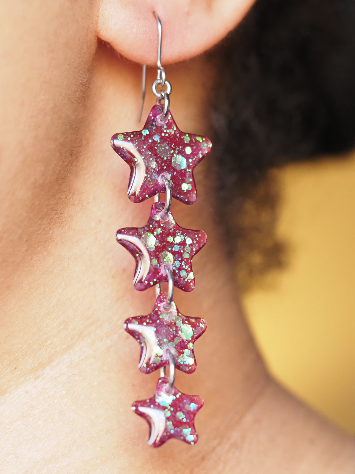 A pair of Astrea star drop earrings, shown being worn. The wearers face is out of shot with hair pulled back to display the earring. 