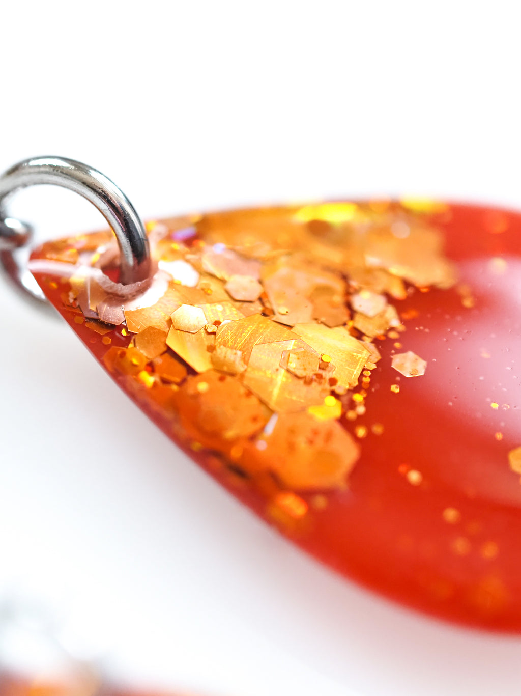 Close up of the Clio earrings in orange with holographic colour shifting glitter on a white background