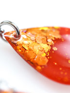 Close up of the Clio earrings in orange with holographic colour shifting glitter on a white background