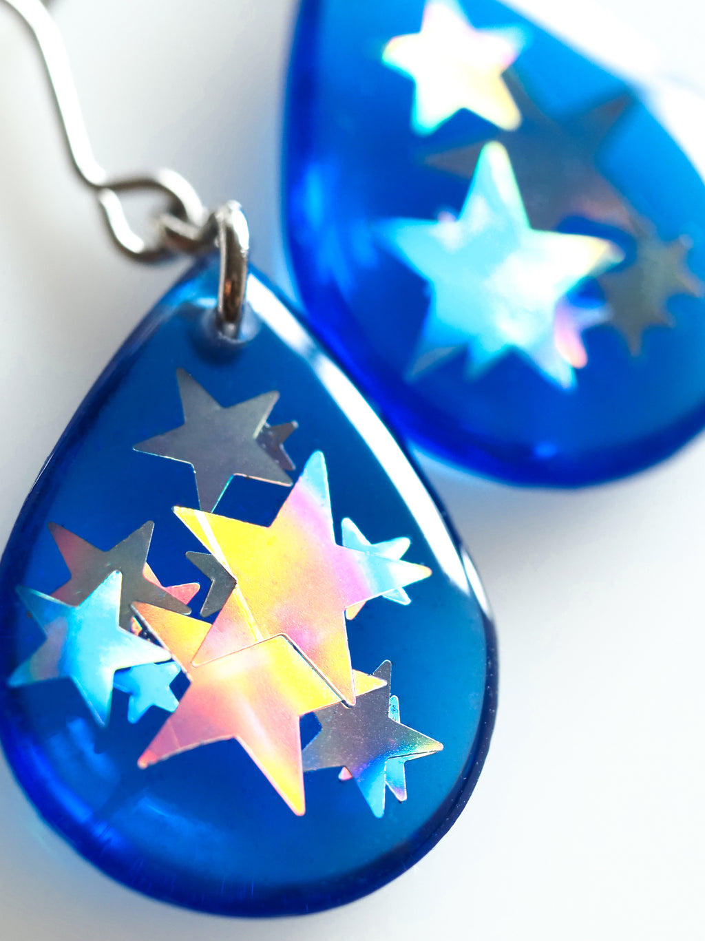 Close up of the Clio drop earrings in transparent blue with holographic star glitter on a white background