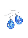 The Clio drop earrings in transparent blue with holographic star glitter on a white background