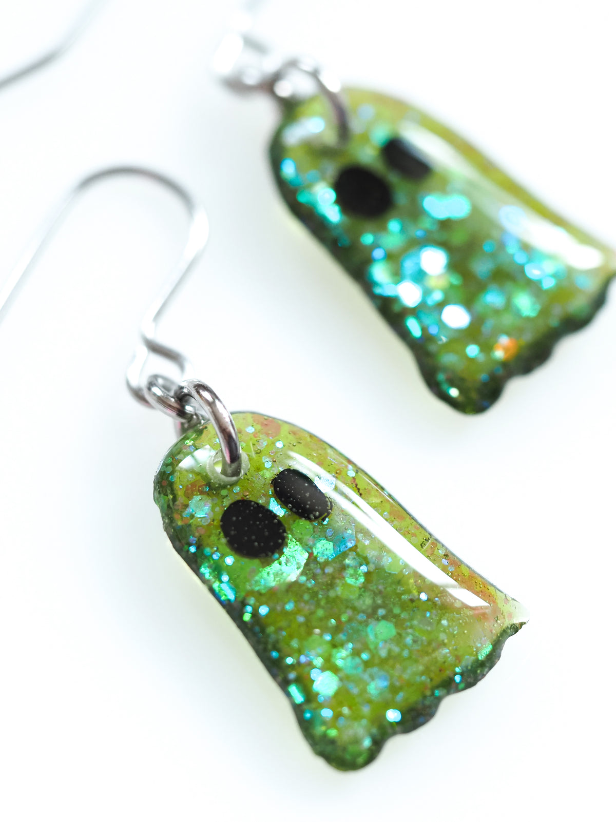 Close up of Ghost drop earrings in green with iridescent colour shifting glitter on a white background