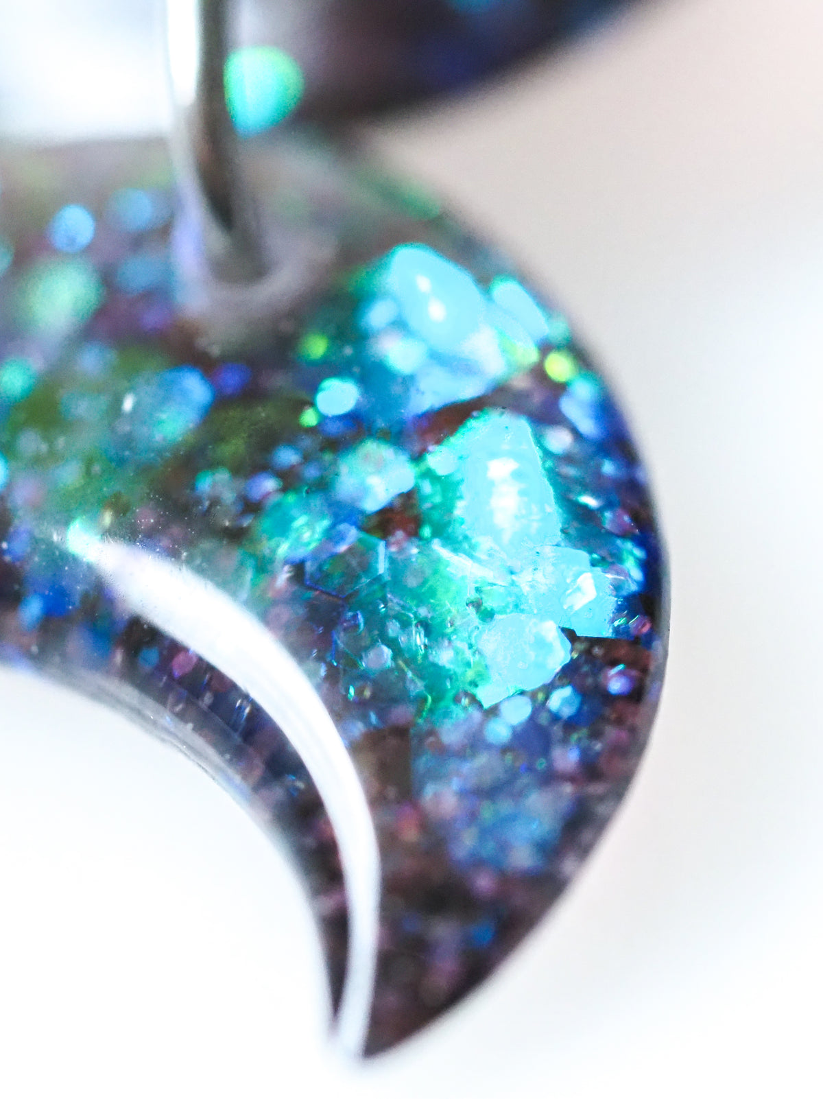 Macro close up of the Hecate triple moon drop earrings in transparent black with iridescent glitter on a white background