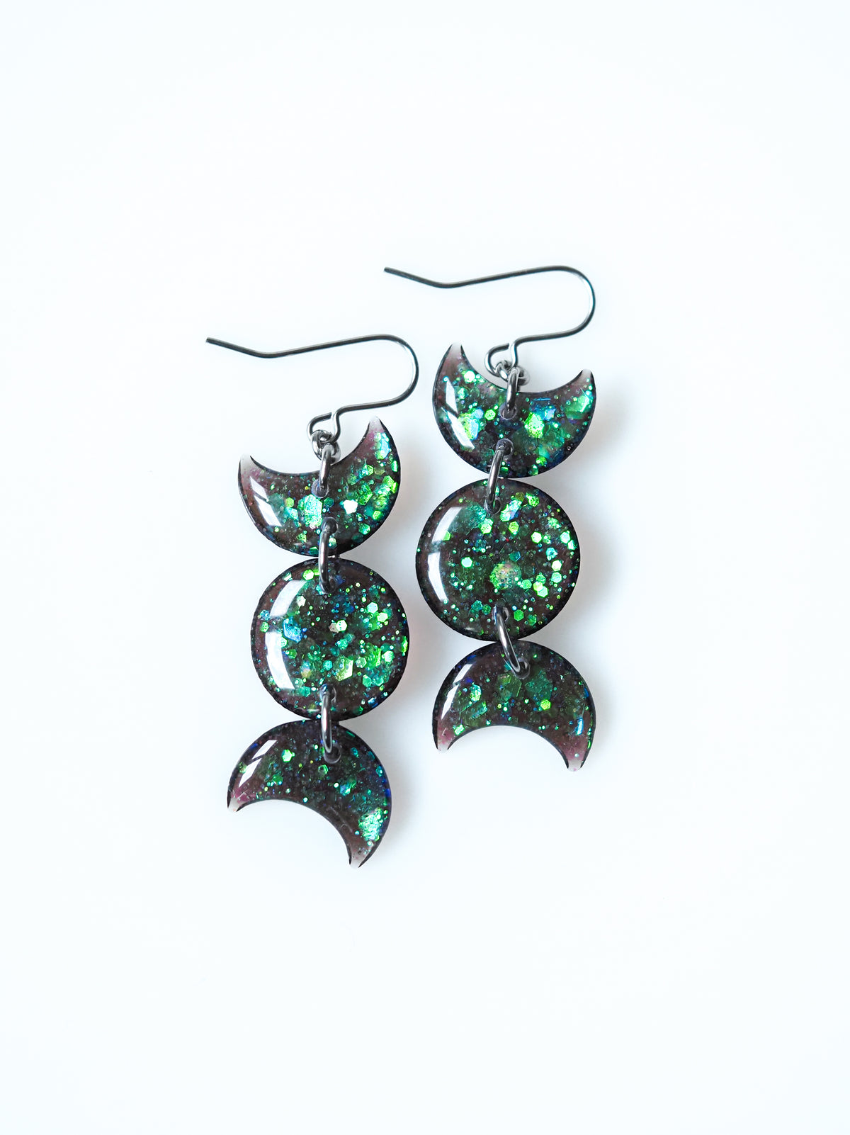 Hecate triple moon drop earrings in transparent black with iridescent glitter on a white background