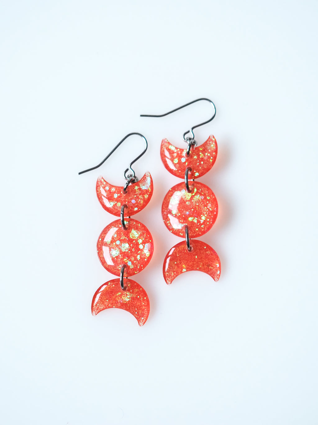 Hecate triple moon drop earrings in transparent orange with iridescent glitter on a white background