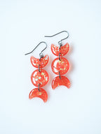 Hecate triple moon drop earrings in transparent orange with iridescent glitter on a white background