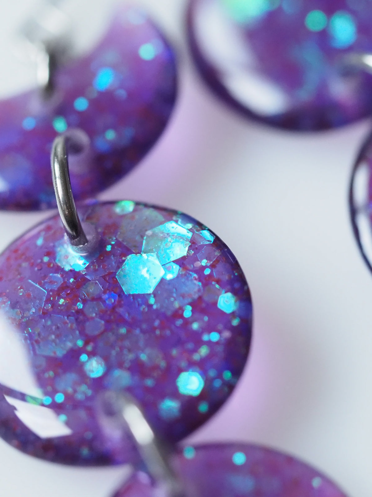 Macro close up of the Hecate triple moon drop earrings in transparent purple with iridescent glitter on a white background
