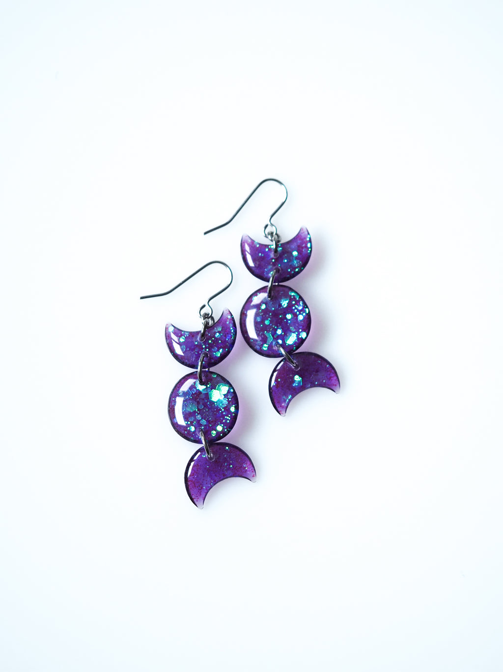 Hecate triple moon drop earrings in transparent purple with iridescent glitter on a white background
