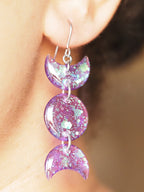 A pair of Hecate triple moon drop earrings, shown being worn. The wearers face is out of shot with hair pulled back to display the earring. 
