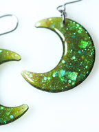 Close up of the Luna moon drop earrings in green iridescent glitter on a white background
