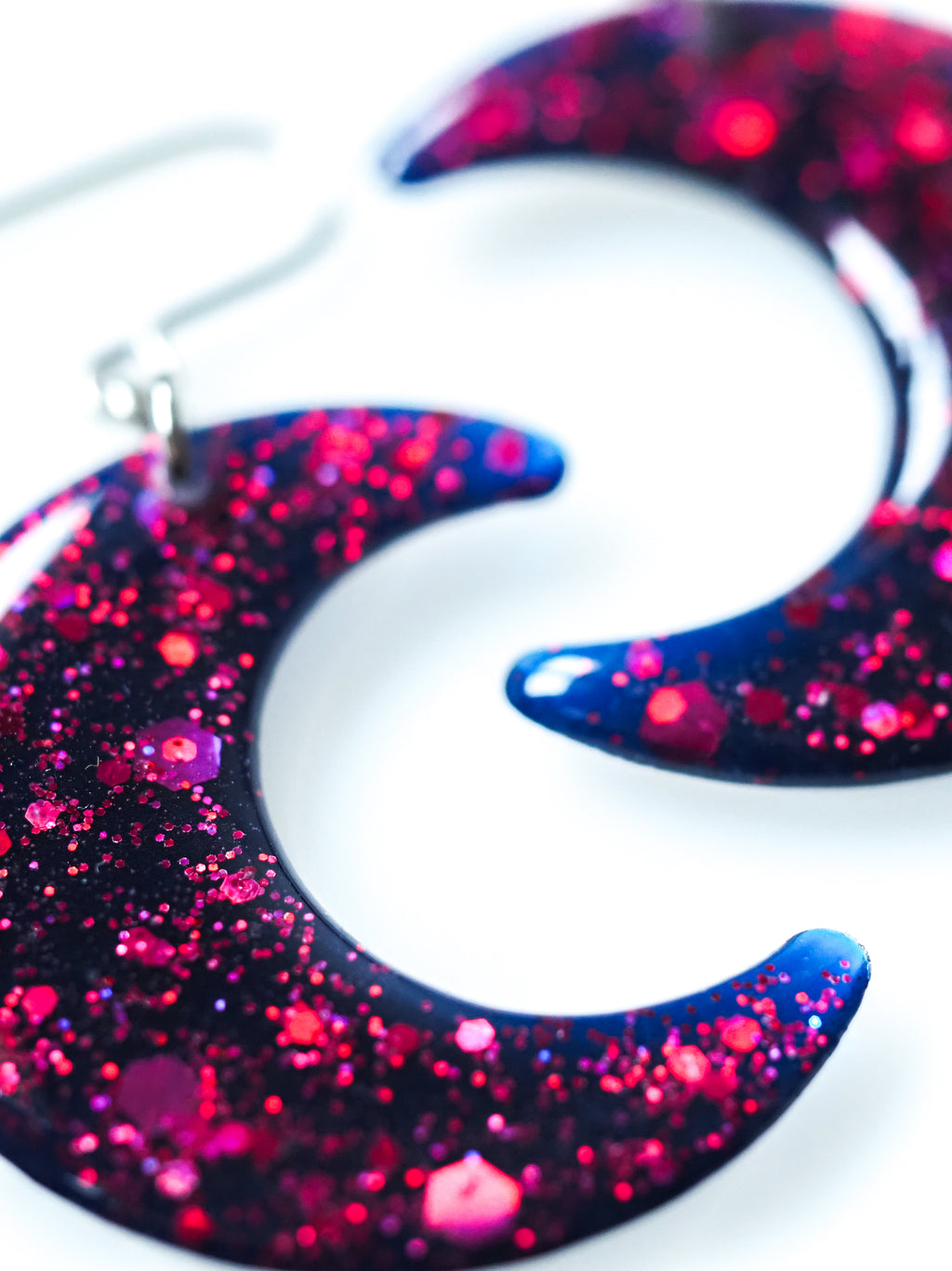Close up of the Luna moon drop earrings in night blue with pink holographic glitter on a white background