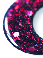 Macro close up of the Luna moon drop earrings in night blue with pink holographic glitter on a white background
