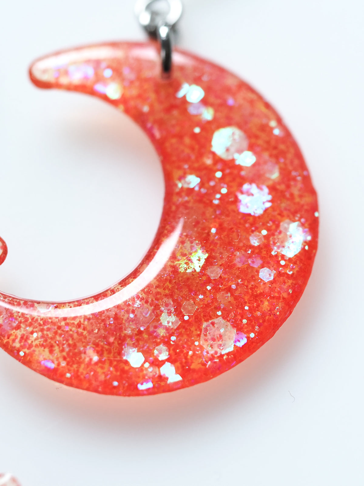 Close up of the Luna moon drop earrings in orange iridescent glitter on a white background