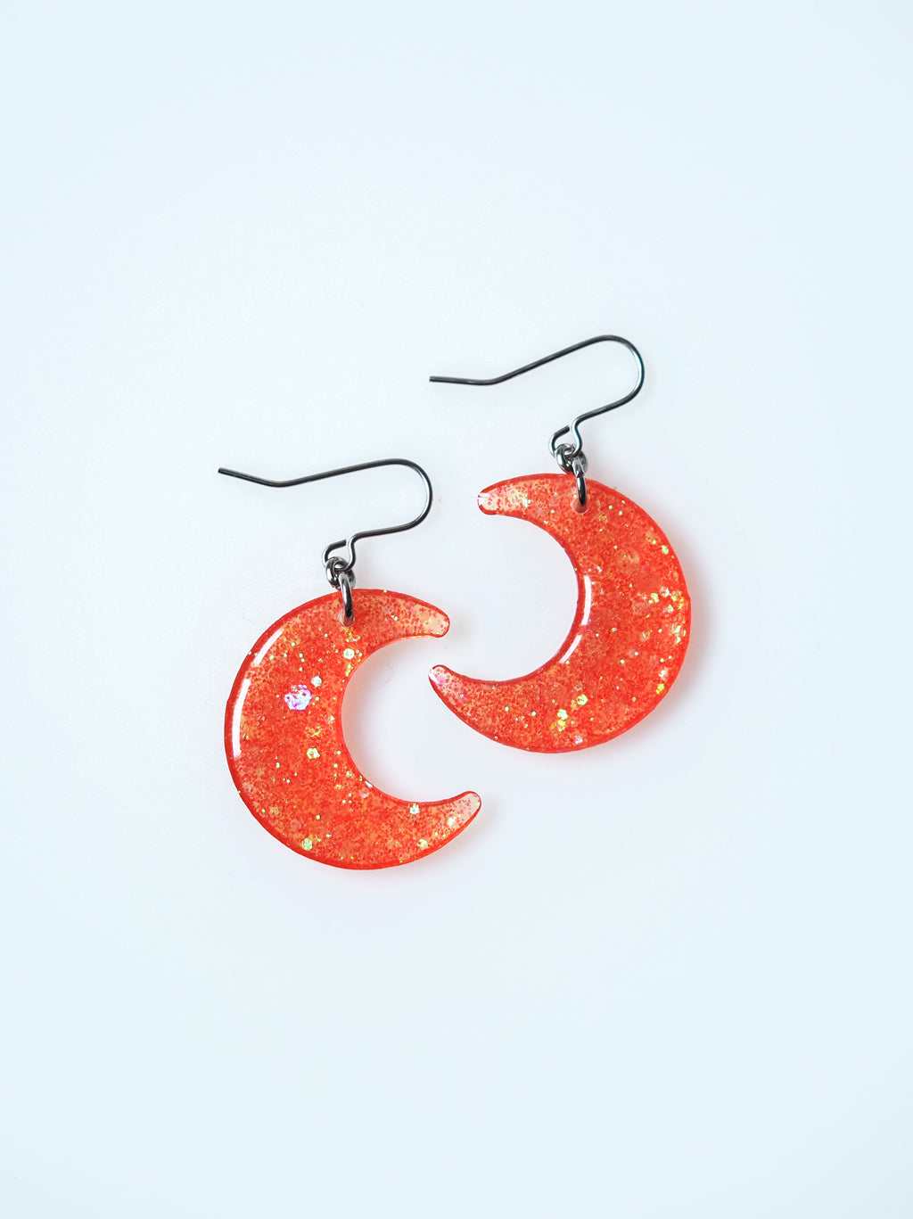 Luna moon drop earrings in orange iridescent glitter on a white background

