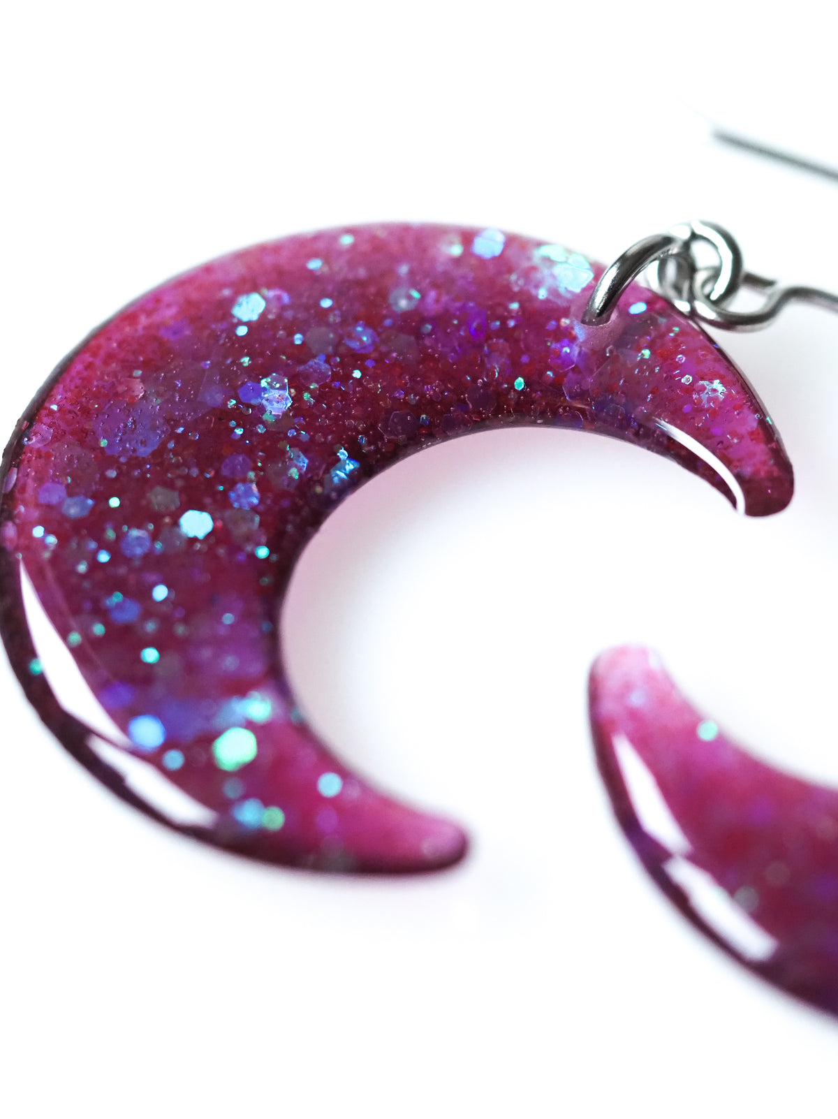 Close up of the Luna moon drop earrings in transparent purple with iridescent glitter on a white background