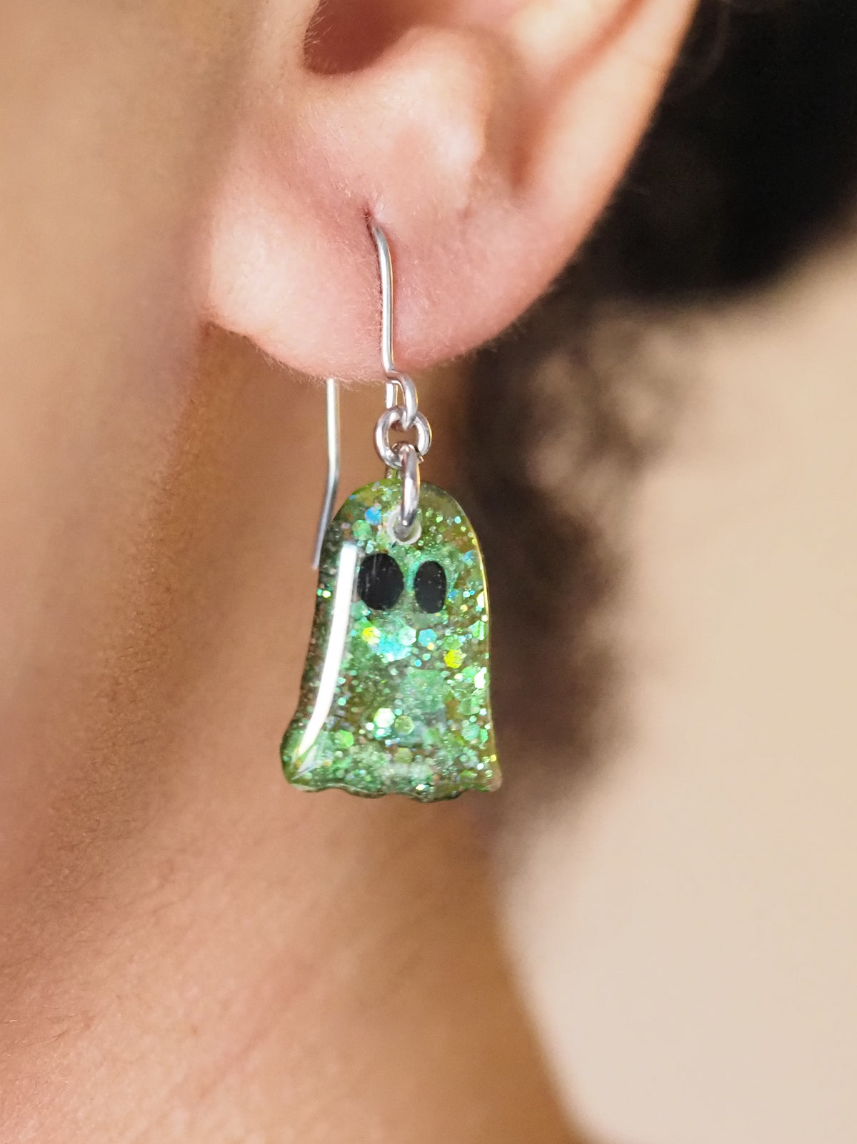 A pair of Melinoe ghost drop earrings, shown being worn. The wearers face is out of shot with hair pulled back to display the earring. 