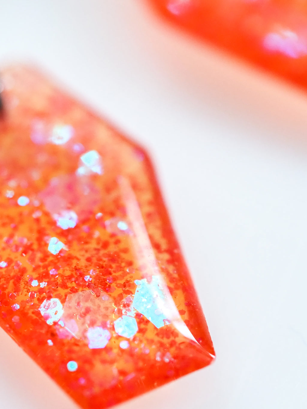 Close up of the Morrigan coffin earrings in transparent orange with iridescent colour shifting glitter on a white background