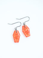 Morrigan coffin earrings in transparent orange with iridescent colour shifting glitter on a white background