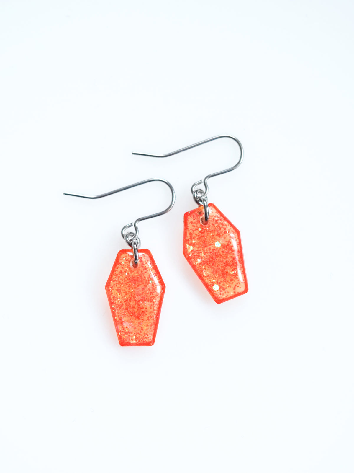 Morrigan coffin earrings in transparent orange with iridescent colour shifting glitter on a white background