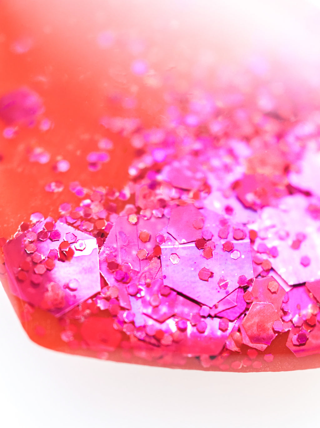 Close up of the Persephone drop earrings in orange with pink holographic glitter on a white background