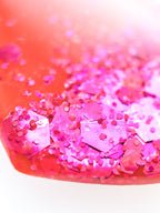 Close up of the Persephone drop earrings in orange with pink holographic glitter on a white background