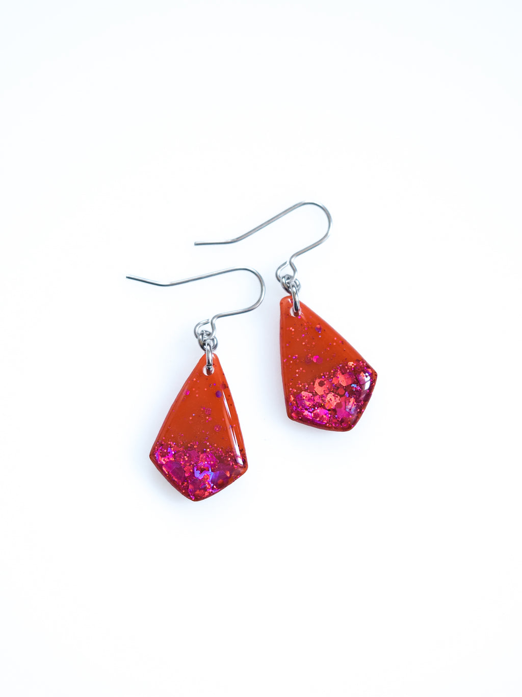Persephone drop earrings in orange with pink holographic colour shifting glitter on a white background