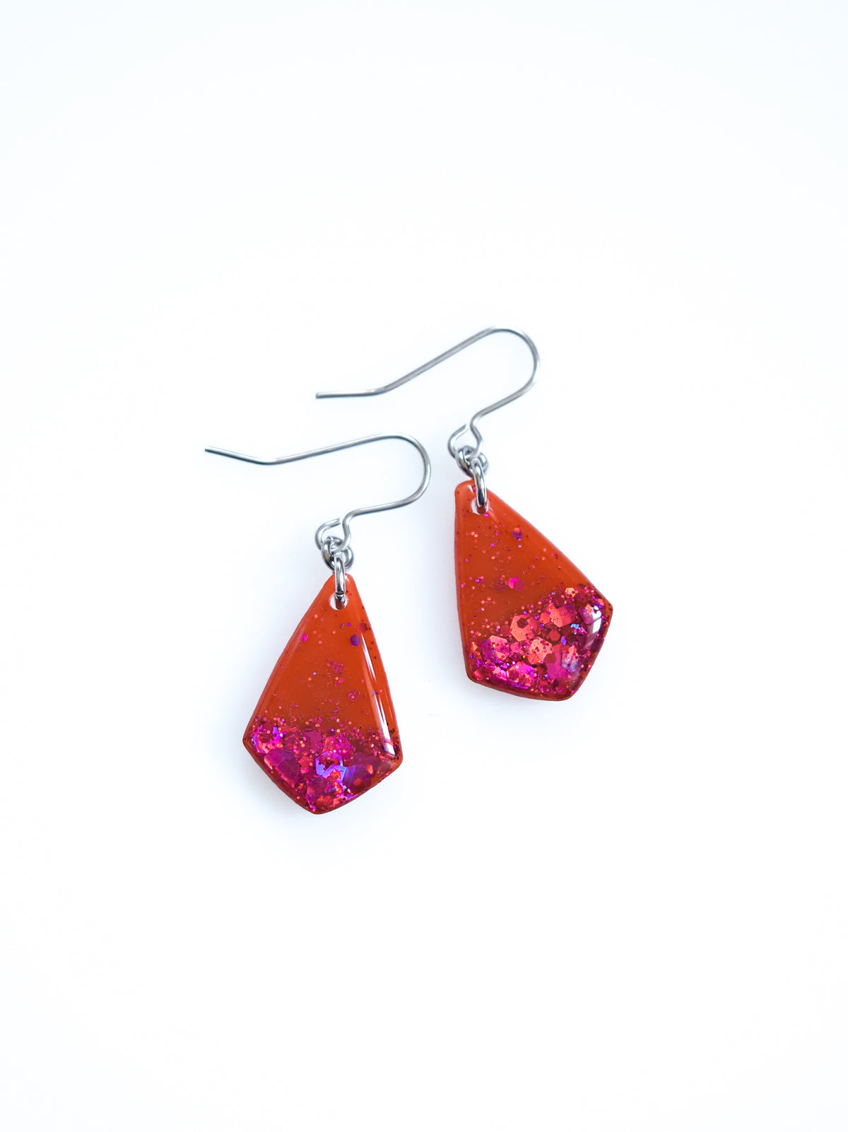 Persephone drop earrings in orange with pink holographic colour shifting glitter on a white background