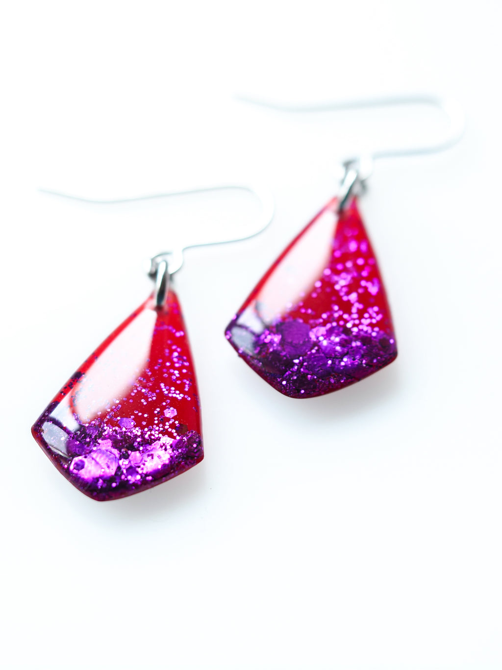 Close up of Persephone drop earrings in red with purple metallic glitter on a white background