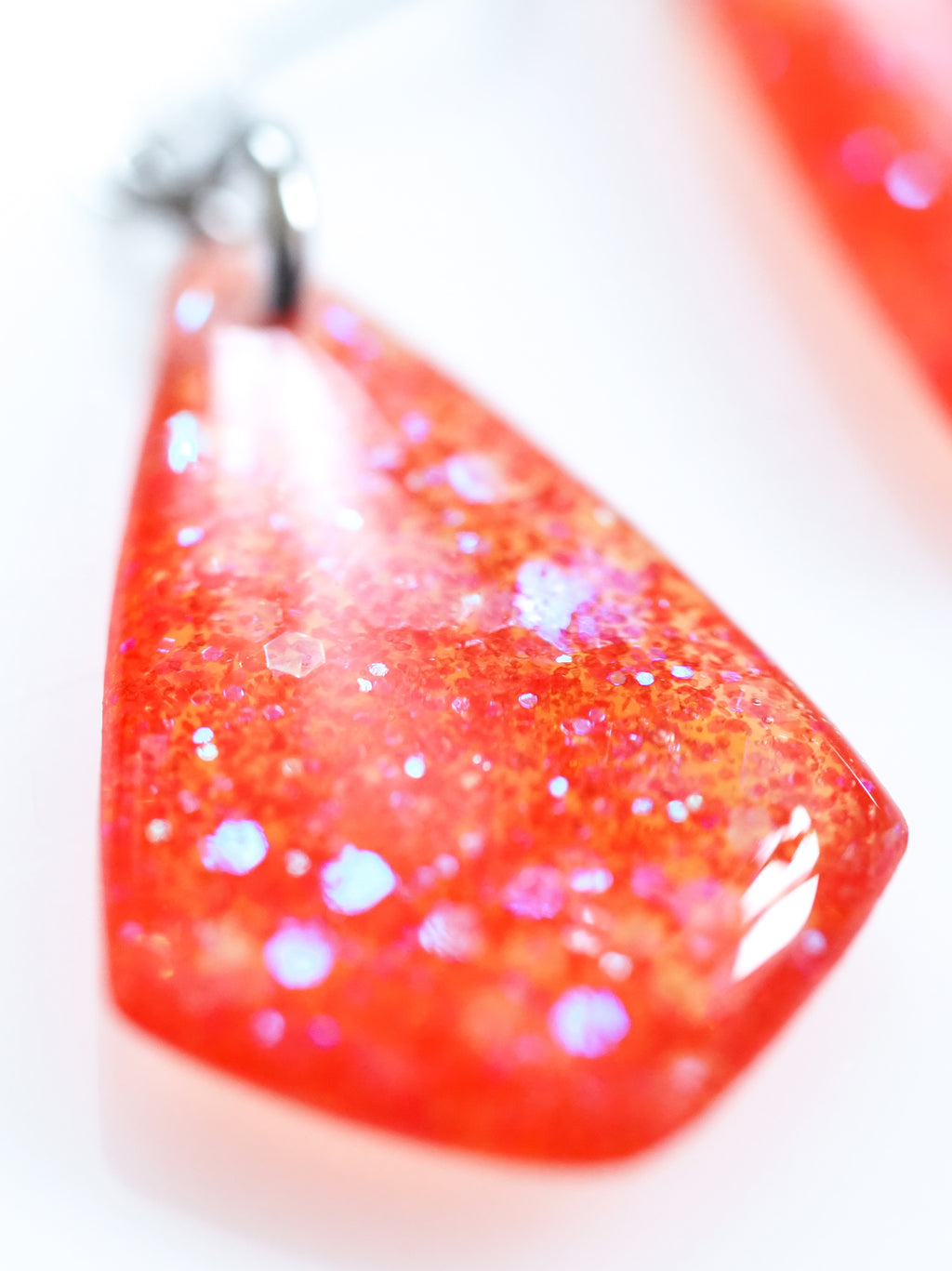 Close up of the Persephone drop earrings in orange with iridescent colour shifting glitter on a white background