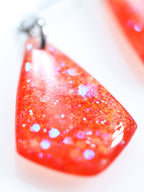 Close up of the Persephone drop earrings in orange with iridescent colour shifting glitter on a white background