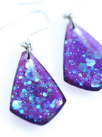 Close up of the Persephone drop earrings in purple with iridescent colour shifting glitter on a white background