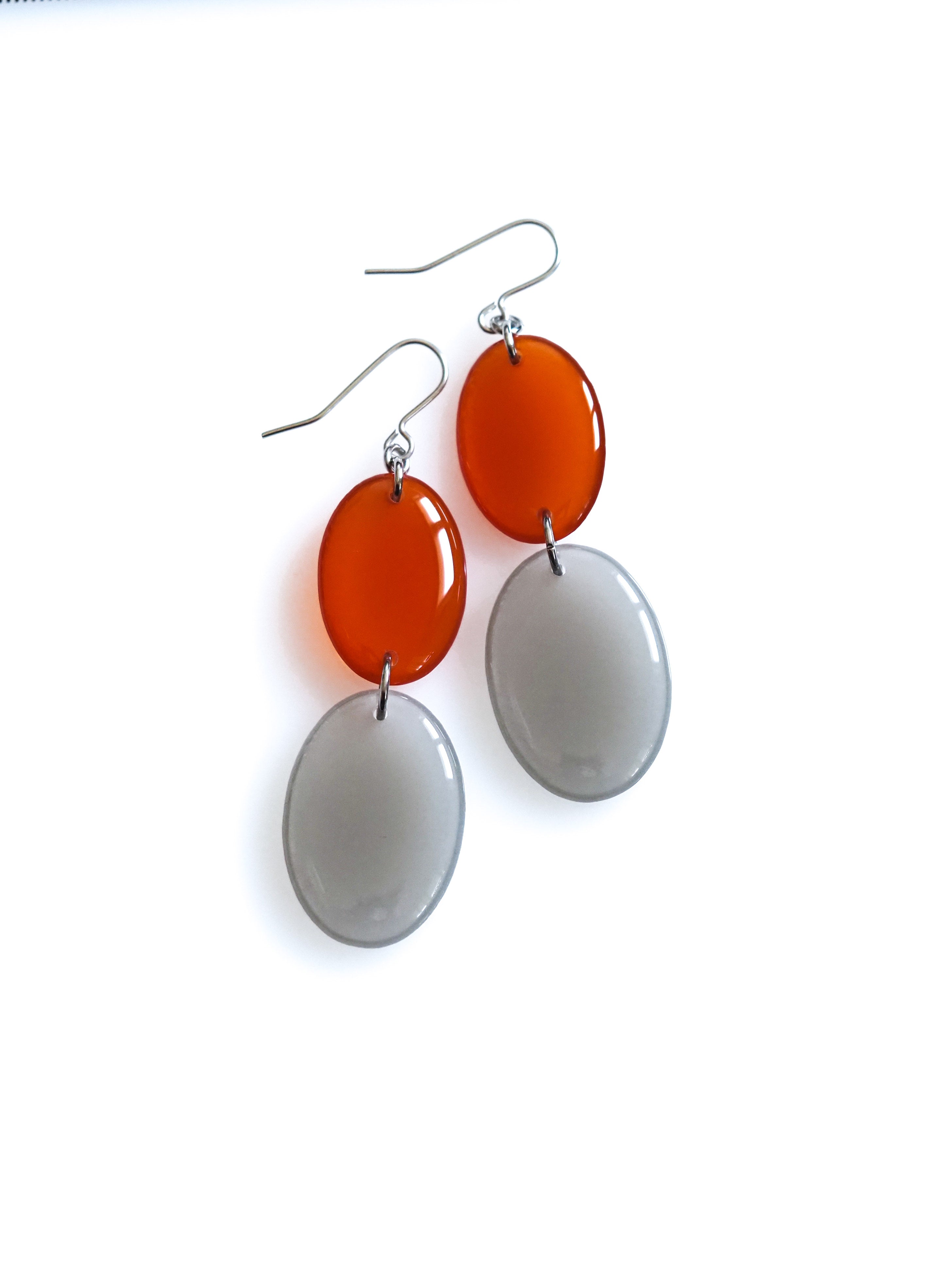 Duet resin drop earrings from the Chroma collection in transparent rust and mist grey on a white background