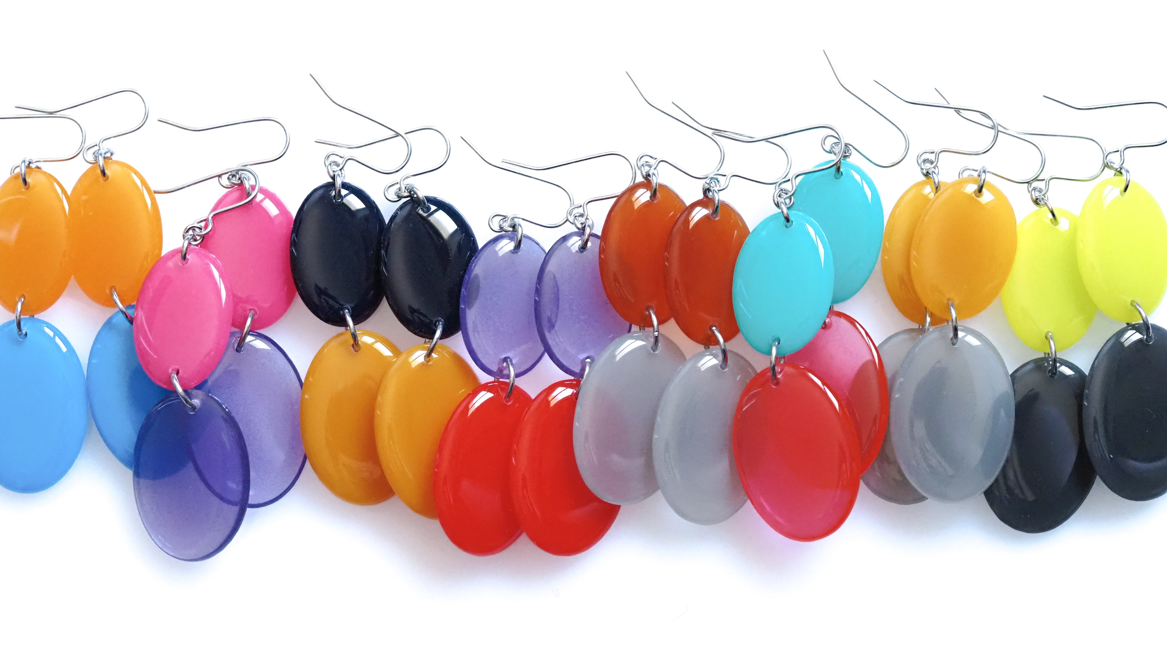 Flat lay photograph of colourful Duet resin earrings from the Chroma collection arranged horizontally on a white background