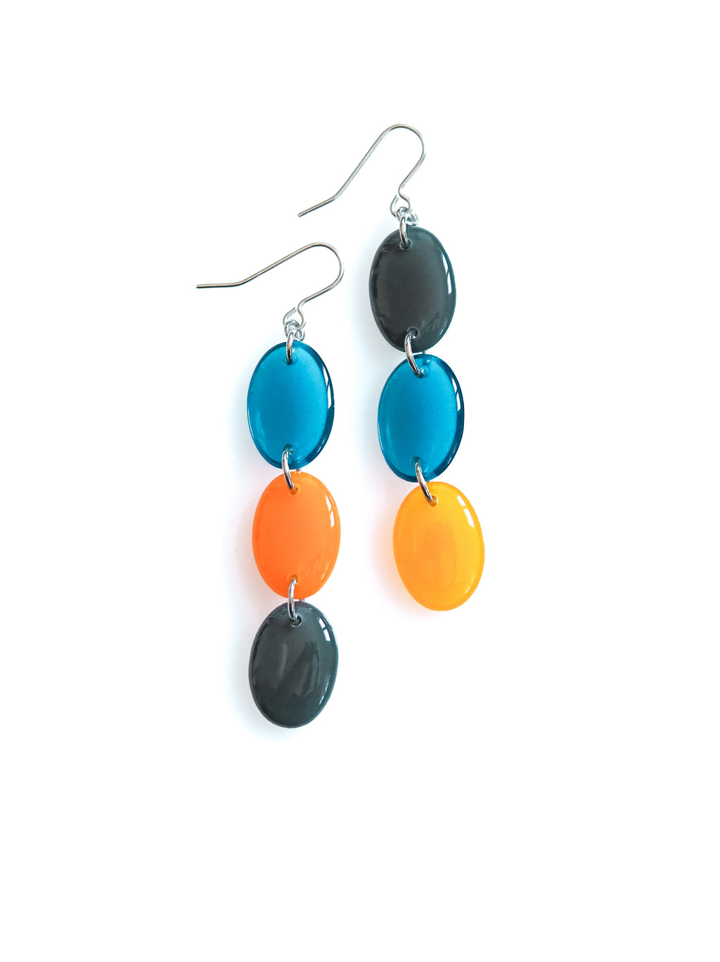 Sequence resin drop earrings from the Chroma collection in transparent ink blue, orange and petrol grey on a white background
