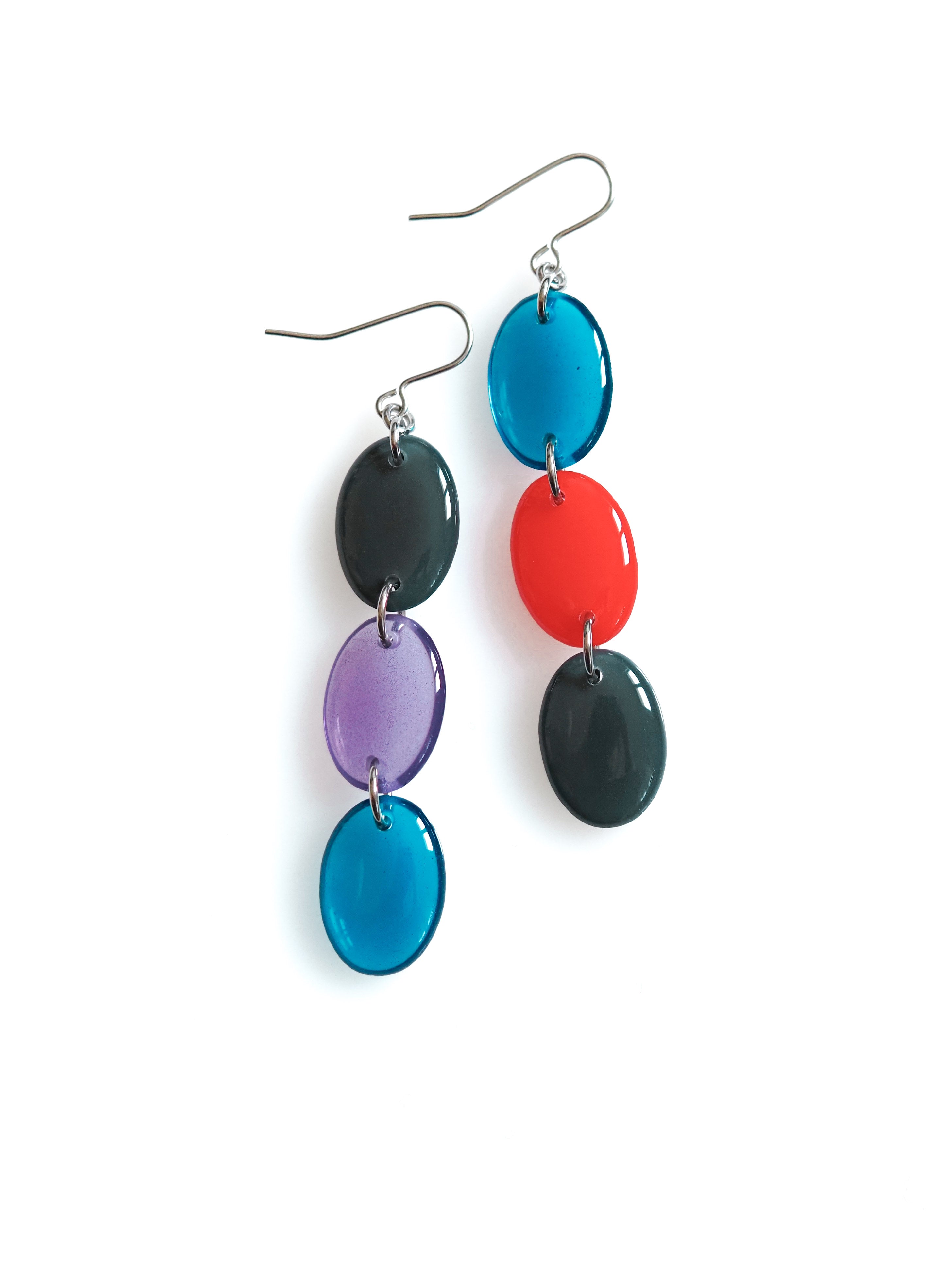 Sequence resin drop earrings from the Chroma collection in petrol grey, transparent aubergine, transparent ink blue and red on a white background