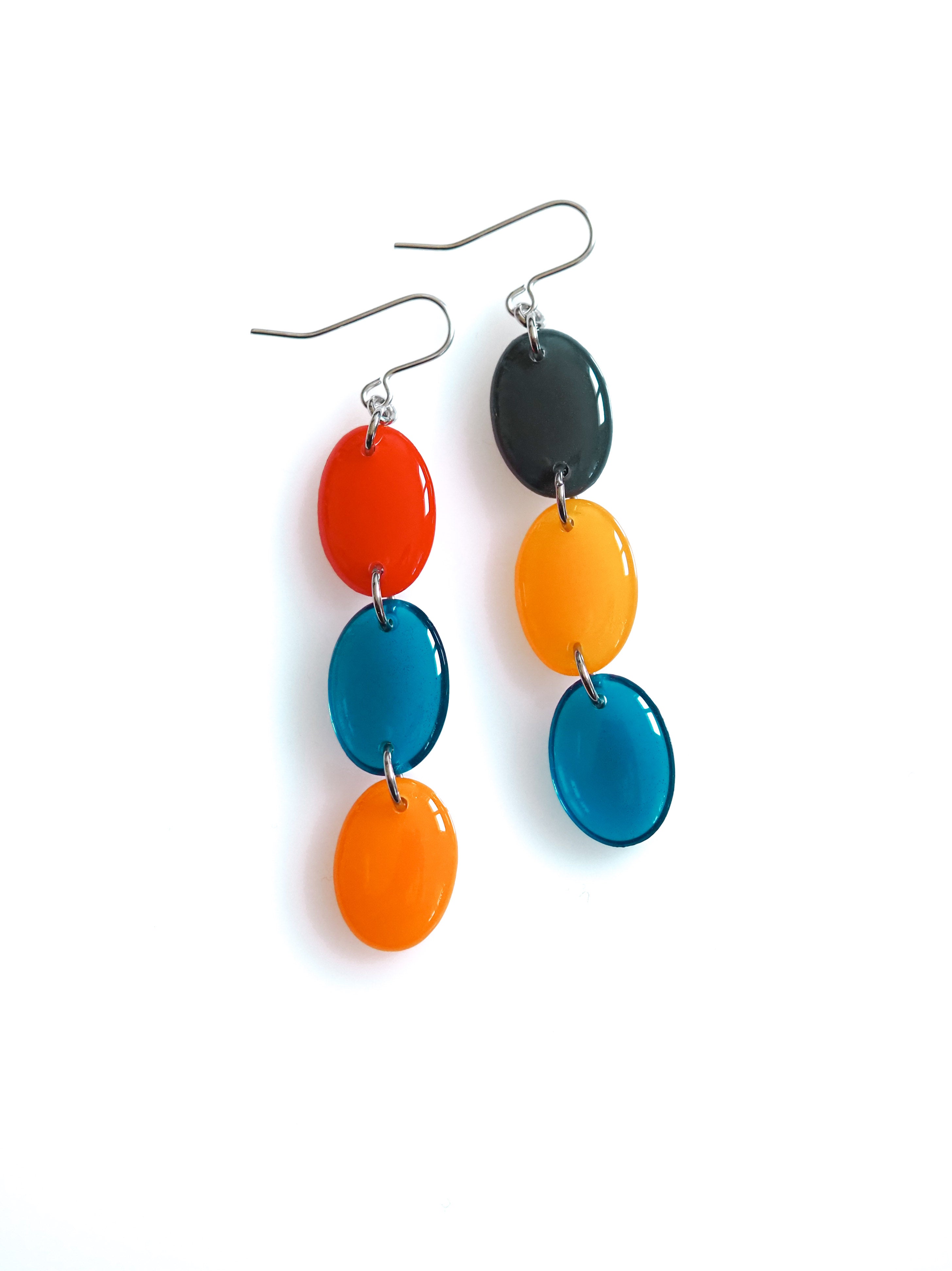 Sequence resin drop earrings from the Chroma collection in red, transparent ink blue, orange, petrol grey and translucent orange on a white background