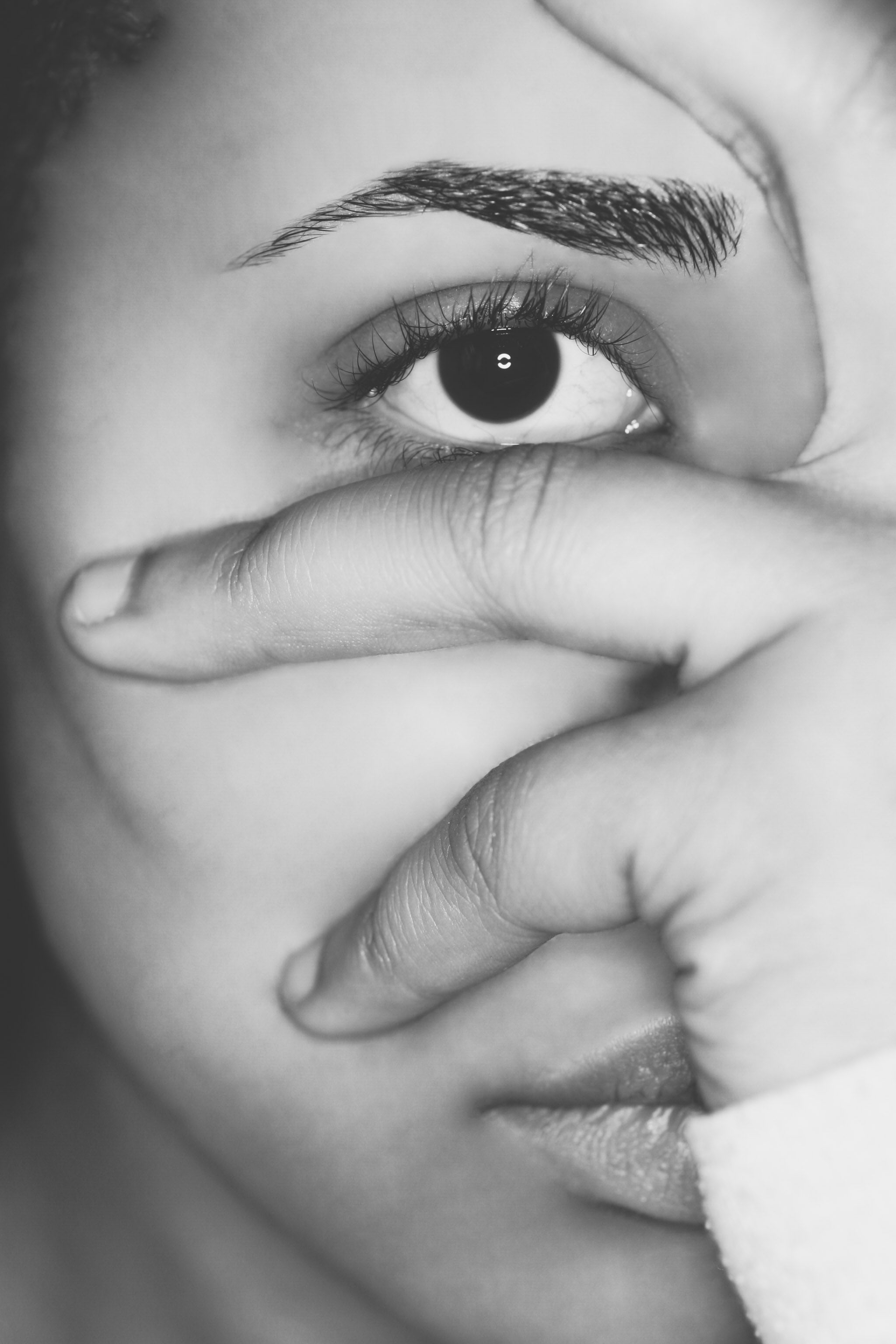 Black and white self-portrait of Micky Leigh, hand hiding most of the face as one eye meets the viewer.