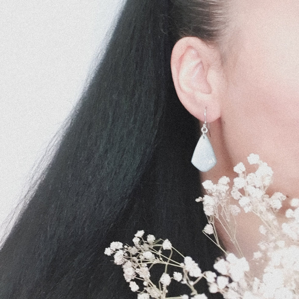 A pair of Persephone drop earrings, shown being worn. The wearers face is out of shot with hair pulled back to display the earring. There are flowers in the foreground.
