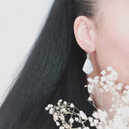 A pair of Persephone drop earrings, shown being worn. The wearers face is out of shot with hair pulled back to display the earring. There are flowers in the foreground.